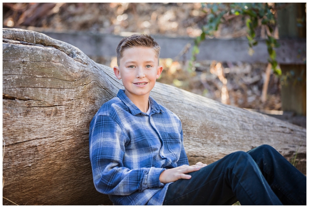 Family portrait session in Orange County. Photograph of the youngest son in the family leaning on a fallen log.