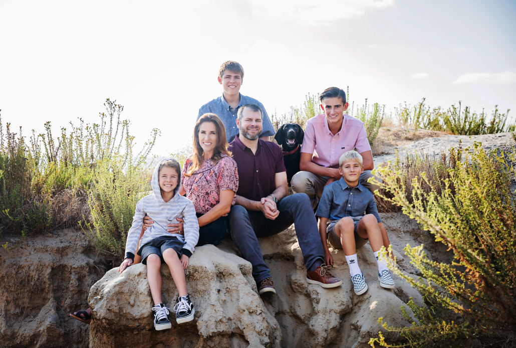 Four sons and their mom and dad in a beach portrait that shows this family of six posing with their pet black lab at San Clemente State Beach. This image including posing ideas with pets at the beach