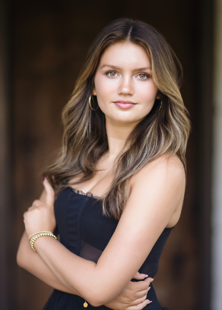Kyra Walsh in a black dress, standing in front of the historic Mission San Juan Capistrano, blending elegance and historical charm in her senior photos