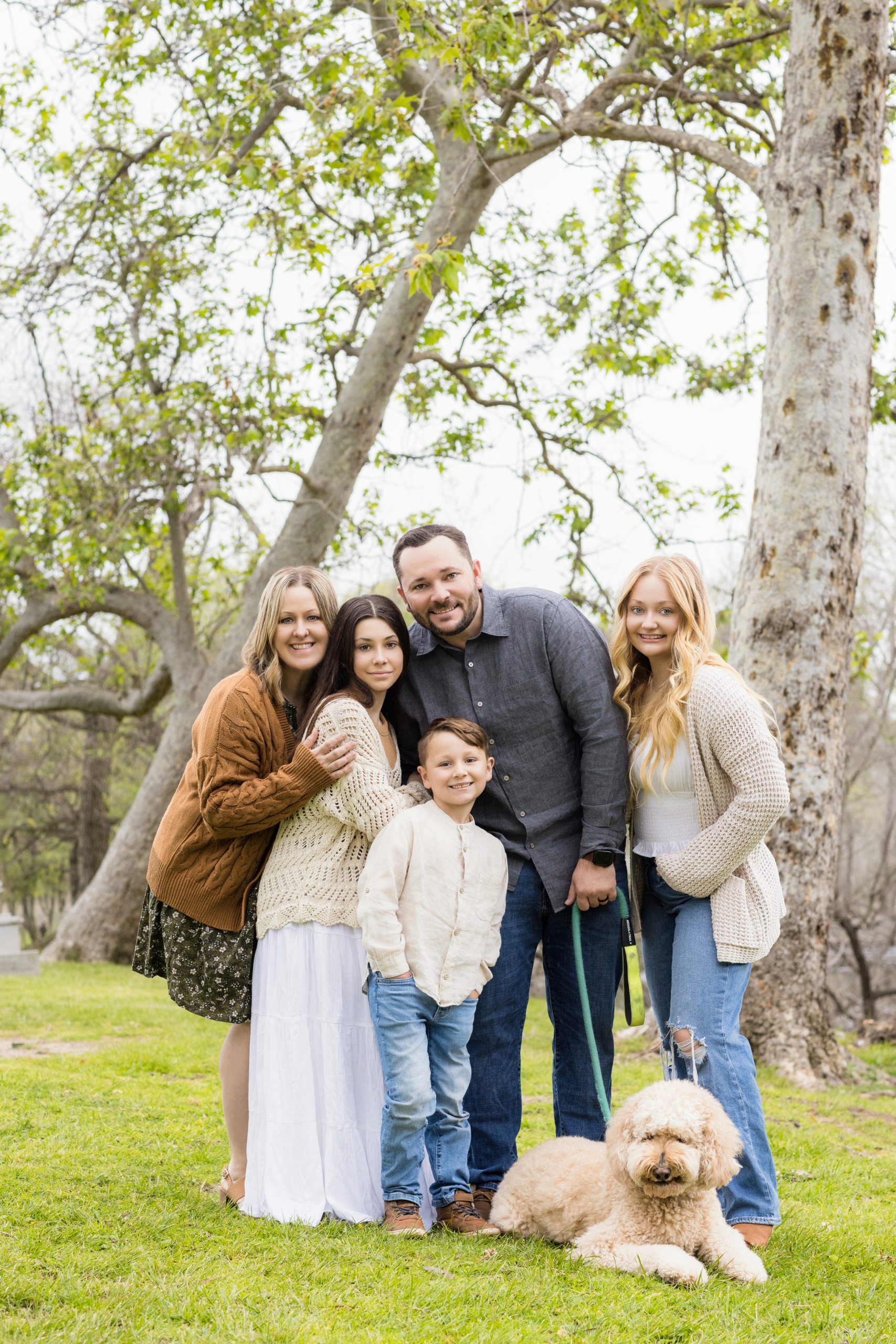 Sweet Family photography session at Huntington Beach Central Park on a cloudy day posing with their white fluffy dog.