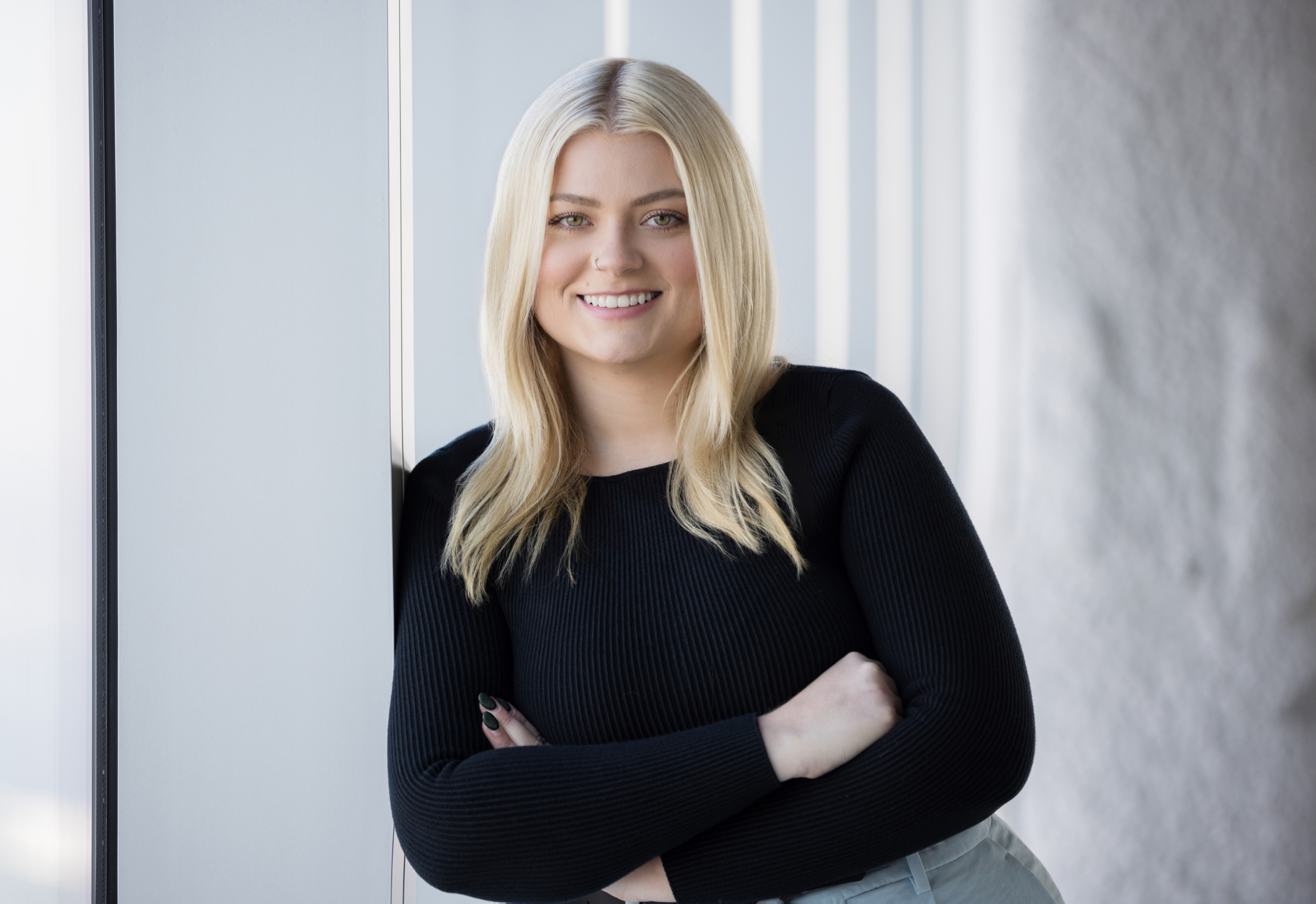 Blonde woman leaning against window with soft natural light. professional corporate headshot with NYC office background