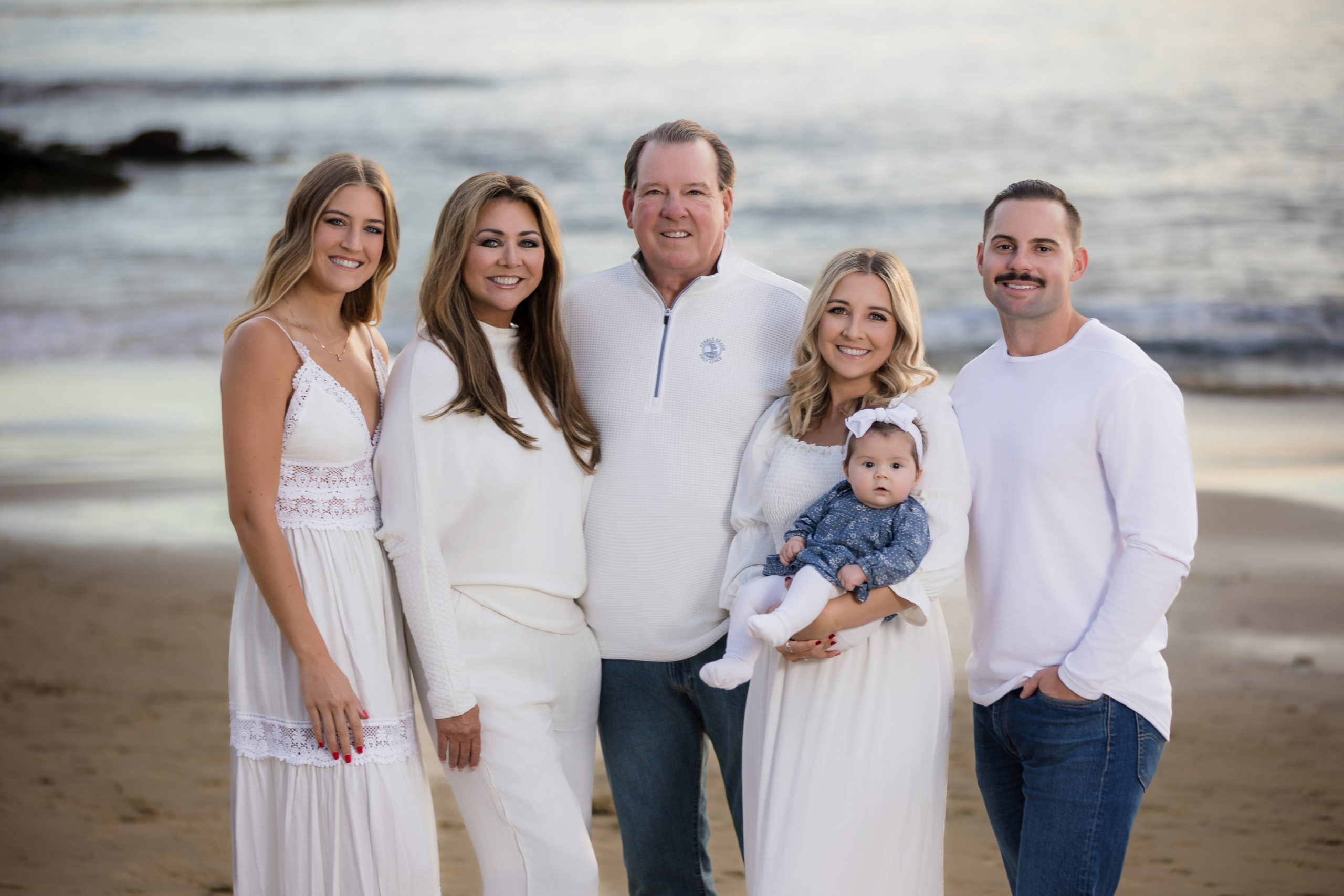 miling multigenerational family posing on the beach at sunset in coordinated white outfits, Laguna Beach family photoshoot.