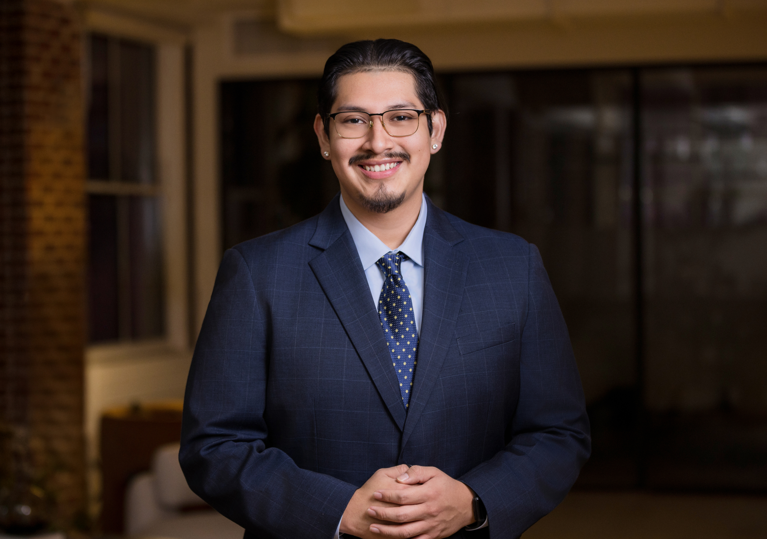 Business professional in navy plaid suit and polka-dot tie smiling in modern office. client wearing classic suit from men’s headshot style guide