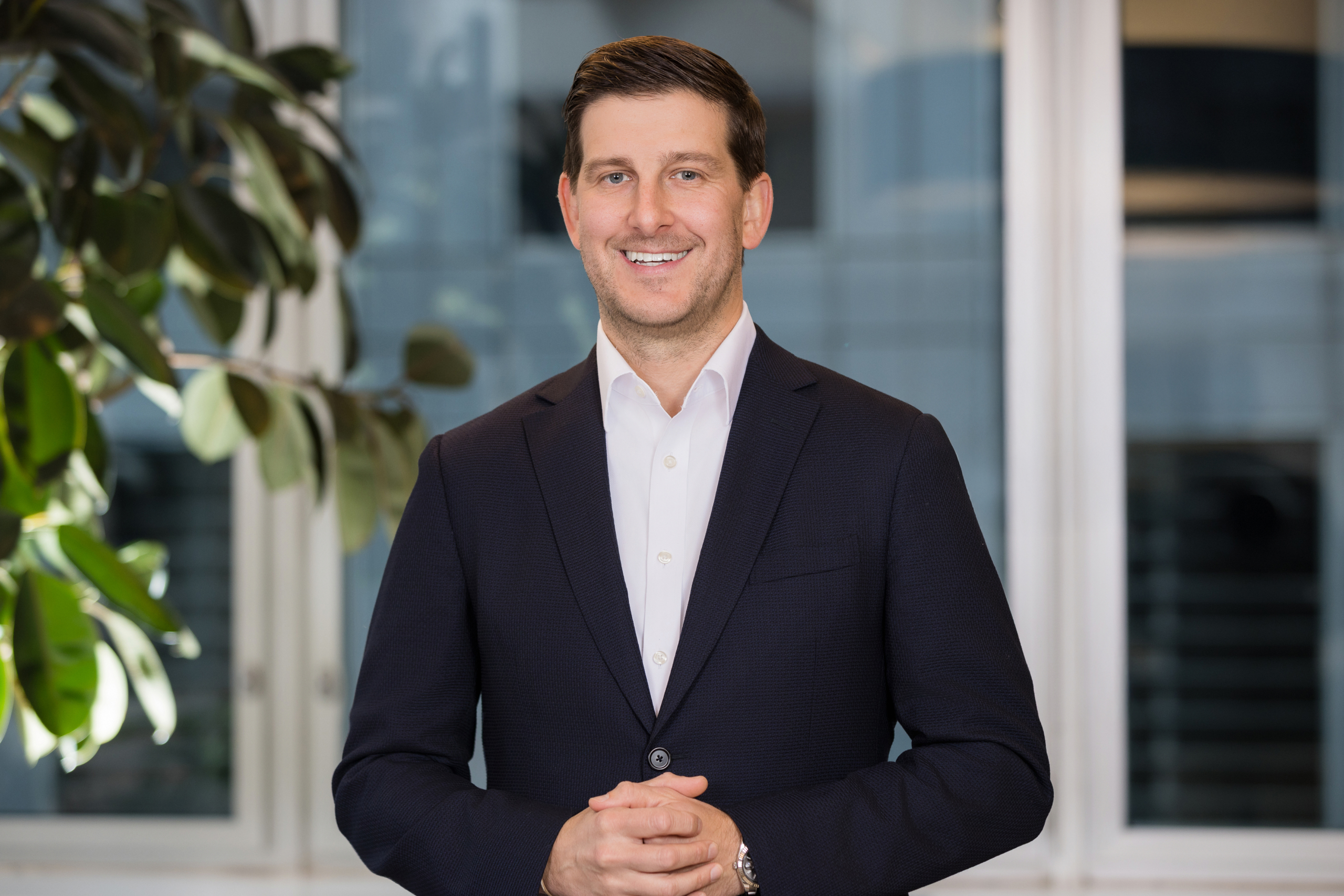 Corporate headshot of man in dark navy suit and white shirt in bright office space. client wearing classic suit from men’s headshot style guide