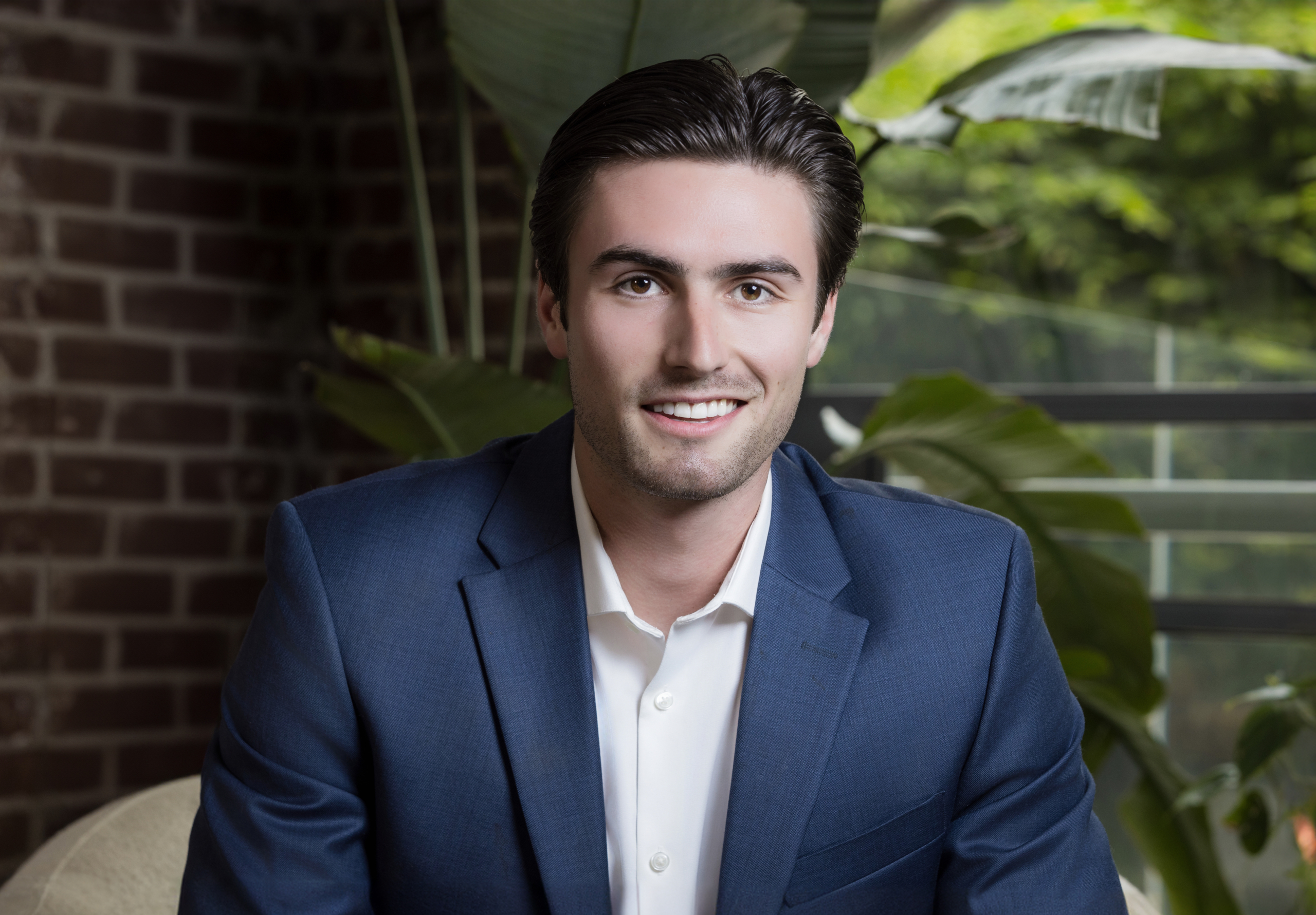 Confident young man in blue suit with open collar shirt in lush indoor setting. client wearing classic suit from men’s headshot style guide