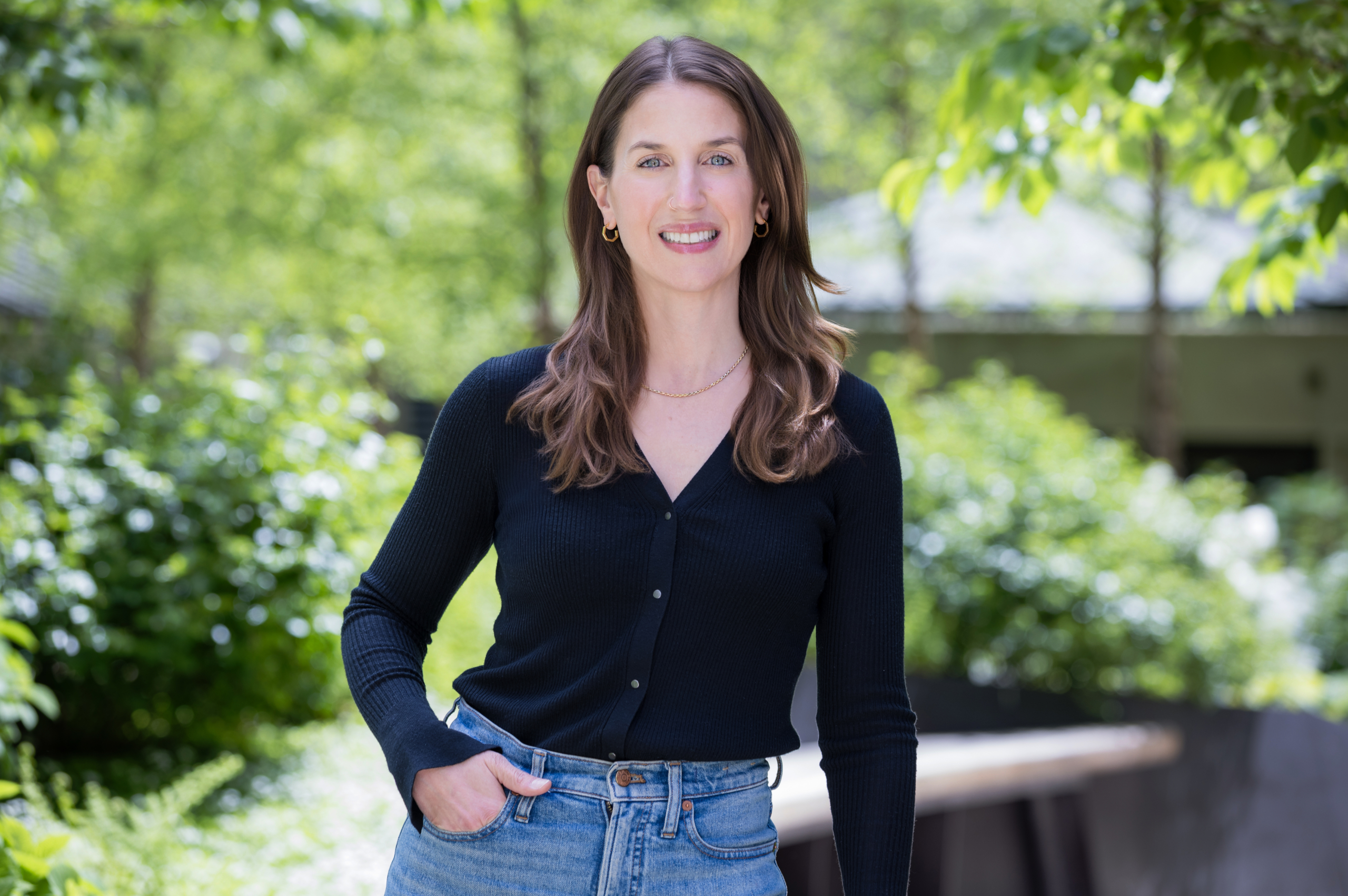 Best corporate headshot backgrounds NYC.Professional woman smiling outdoors with blurred trees in background