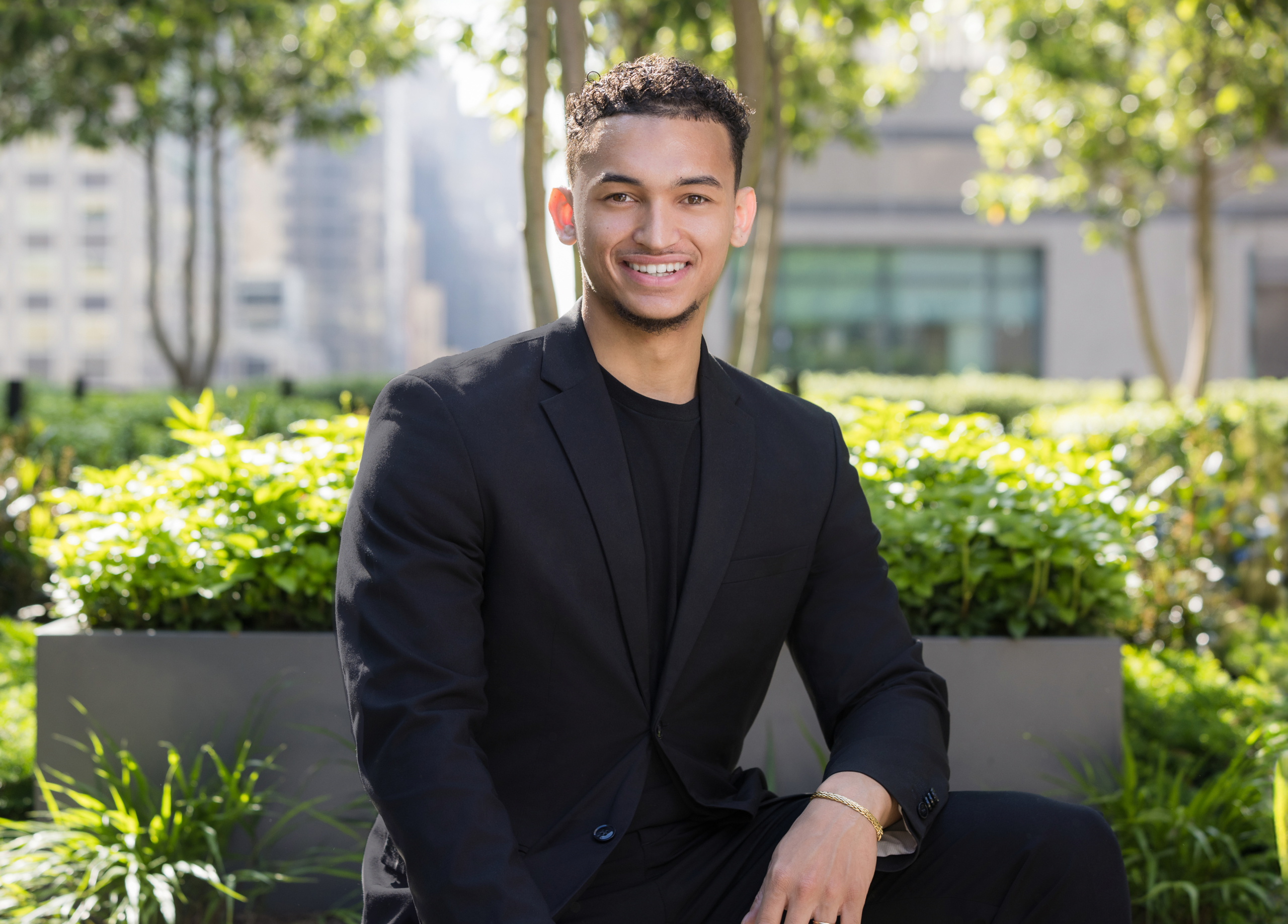 Stylish outdoor headshot of young man in black blazer and crewneck shirt. client wearing classic suit from men’s headshot style guide
