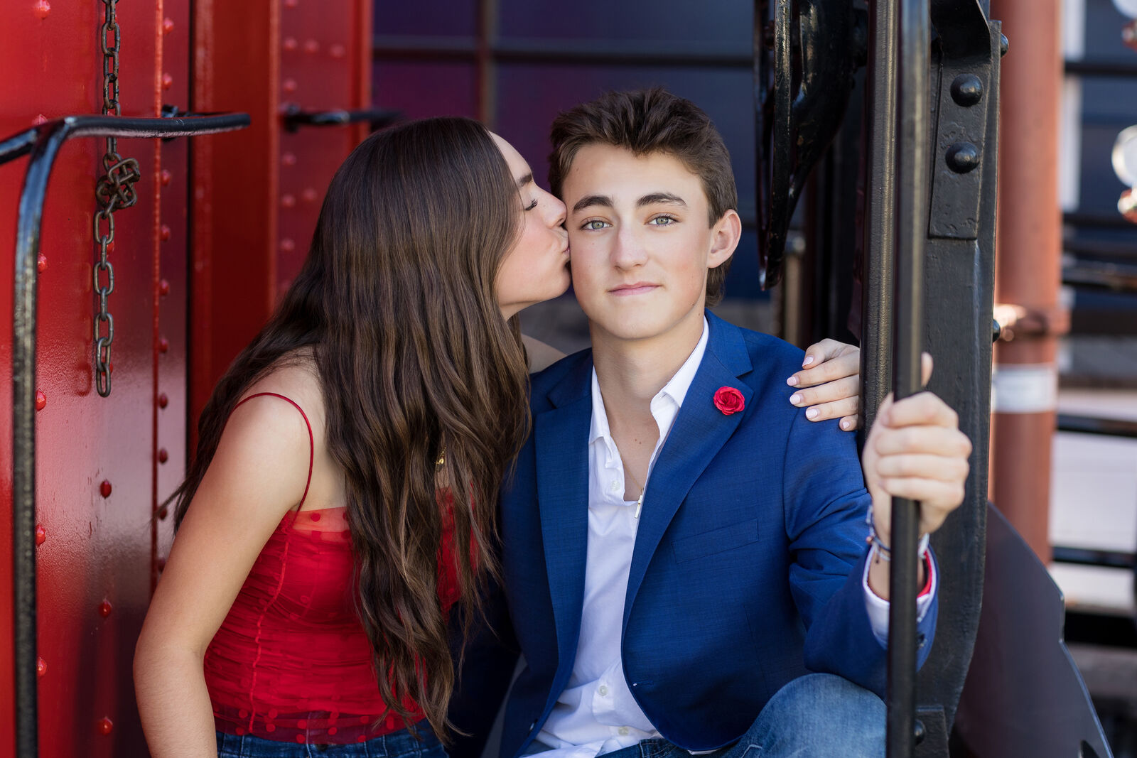 Teenage boy in a navy blazer stepping onto a red vintage train engine near San Juan Capistrano.