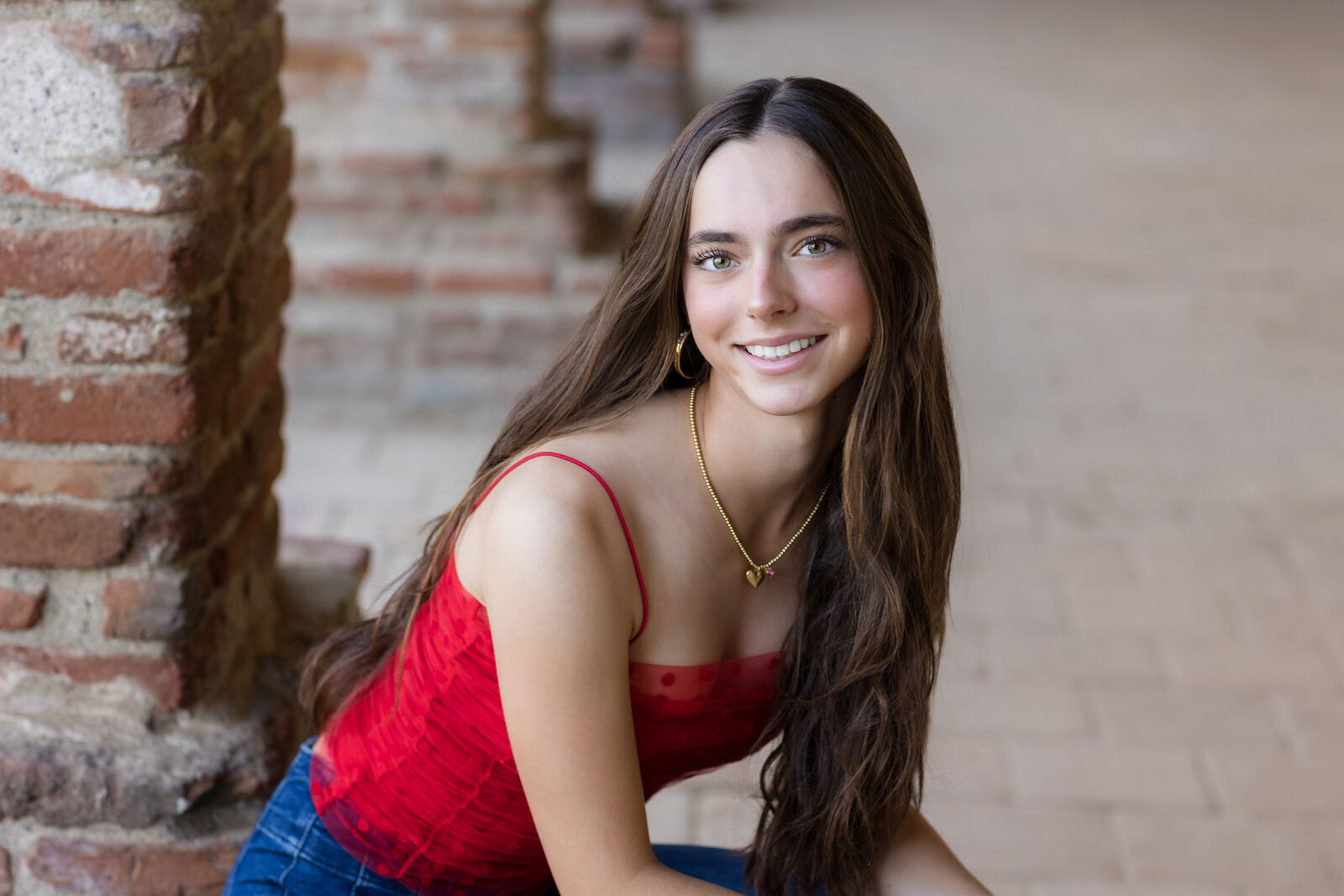 Teenage girl in a red top seated against a warm stone wall at Mission San Juan Capistrano.