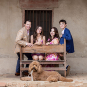 mission-san-juan-capistrano-family-photos-with-dog Family of four with their doodle relaxing on a wooden bench against an adobe wall at the Mission.