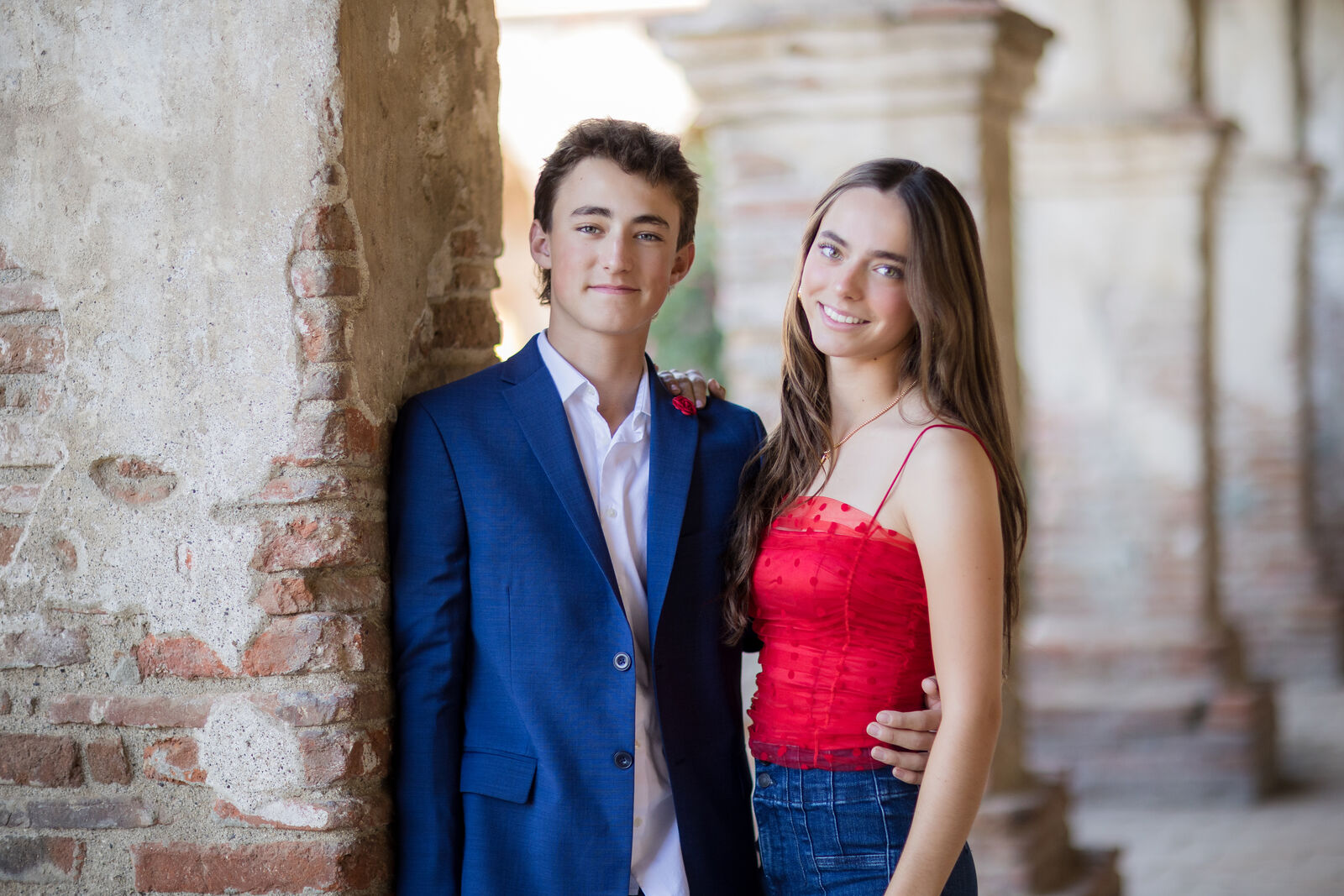 Brother and sister in red and navy holiday outfits standing by a Mission pillar.