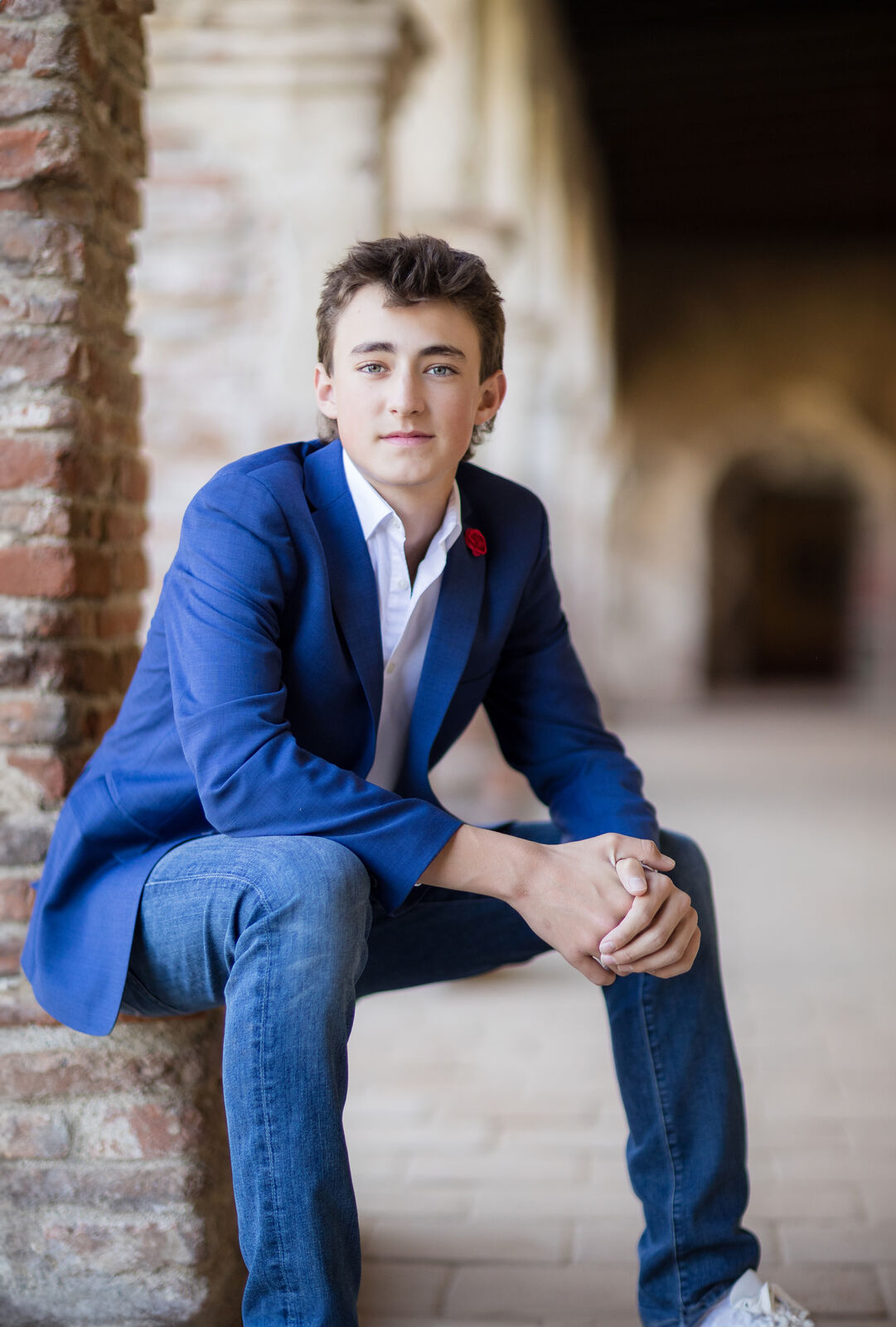 Teen boy in a navy blazer seated in the arched corridor of Mission San Juan Capistrano.