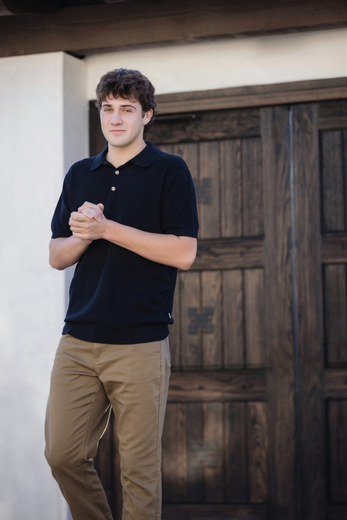 Senior guy in a navy knit polo standing by a carved Spanish wood door in San Clemente