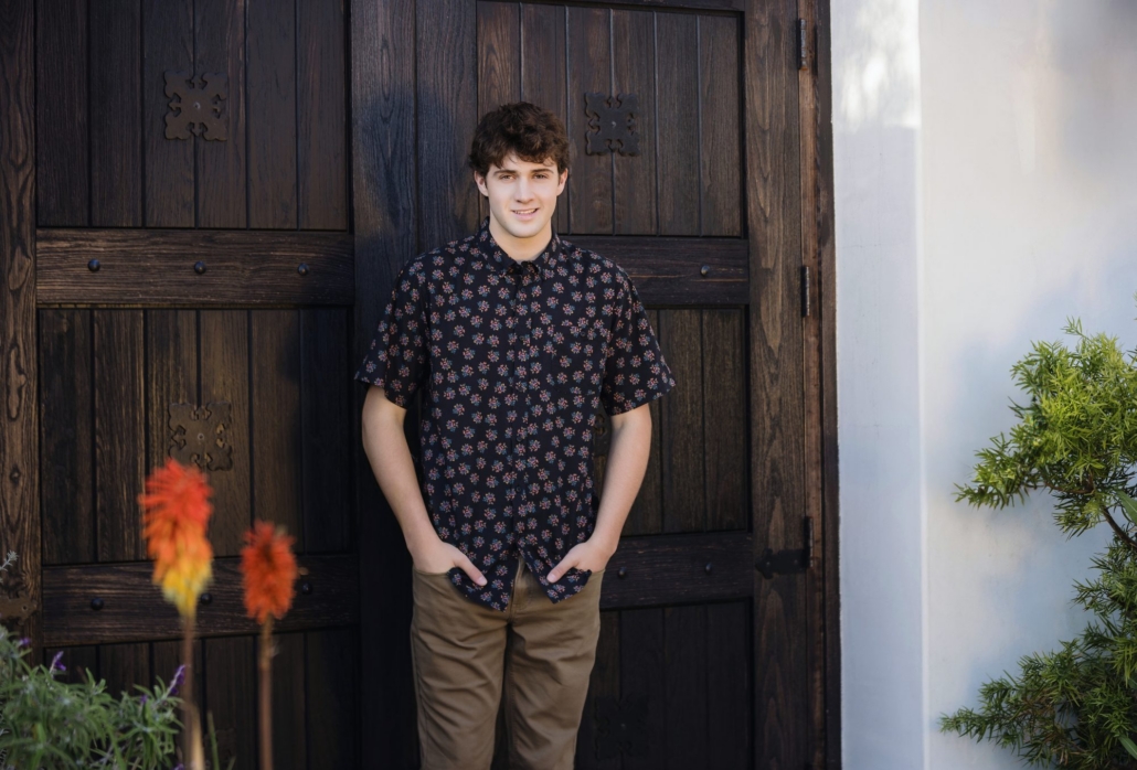 Senior guy in a printed shirt by a carved wood door with flowers in San Clemente