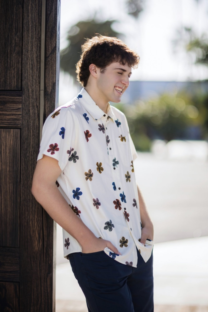 San Clemente urban senior photo of a guy laughing against a wood wall with palm trees behind