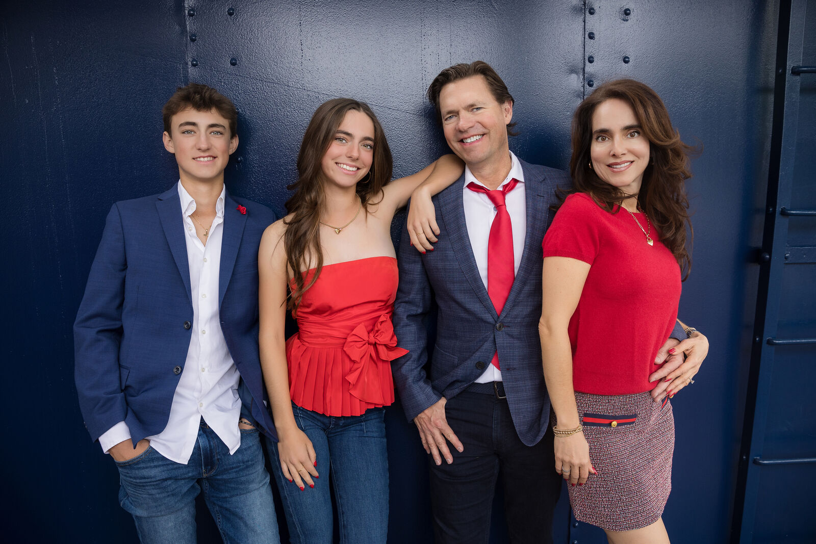 Close family portrait in coordinated red and navy holiday outfits against a deep blue train car.