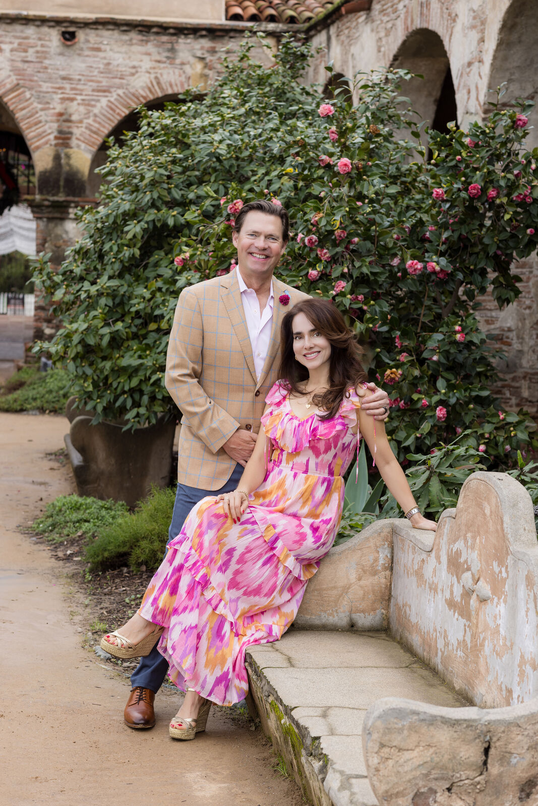 Parents seated together on stone steps beside pink bougainvillea at the Mission.