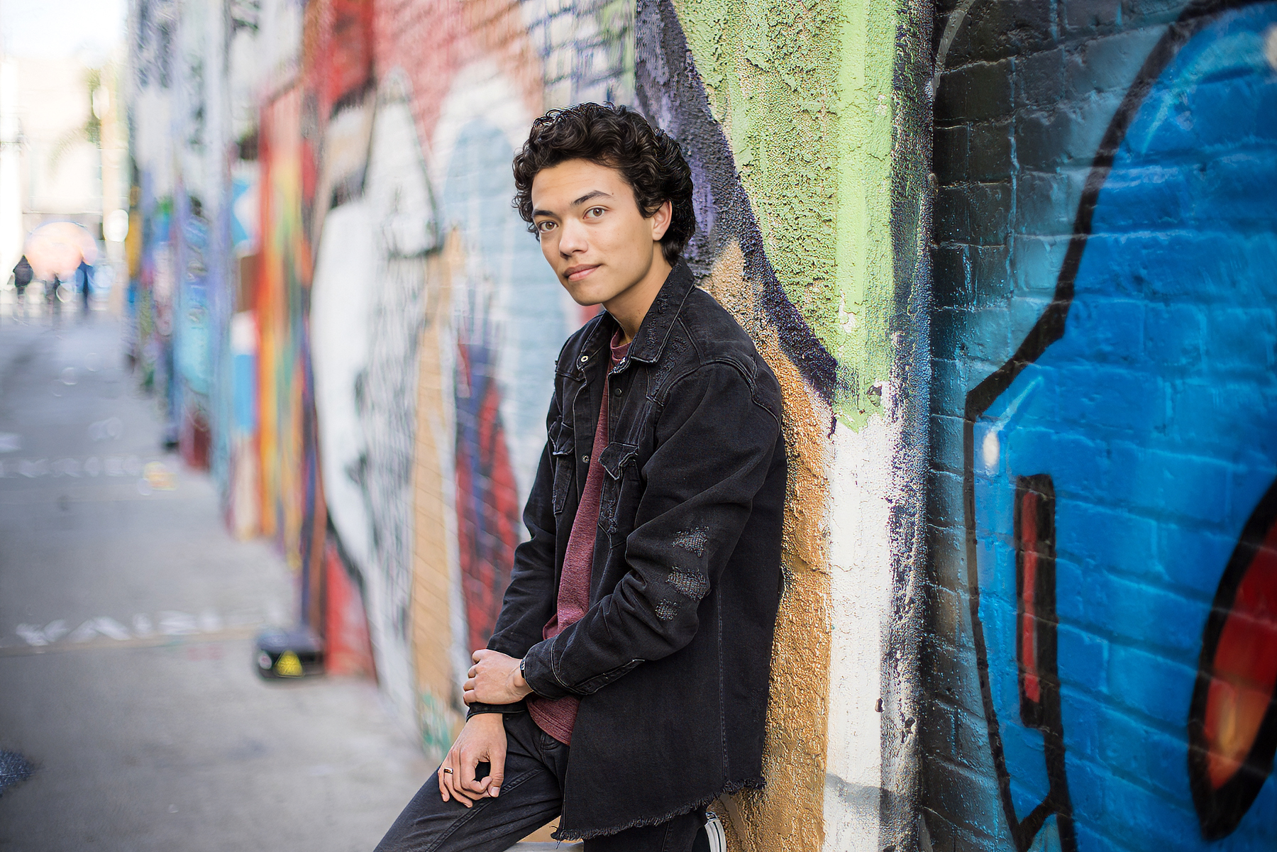 Senior in a structured jacket posing against a textured downtown wall in Orange County.
