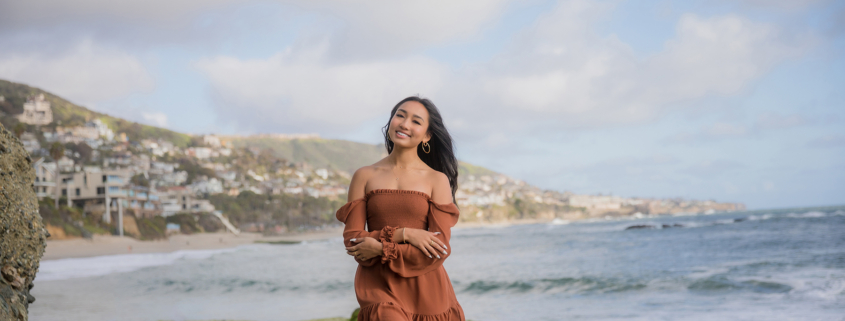 High school senior in a soft neutral outfit posing at golden hour on the Orange County coa